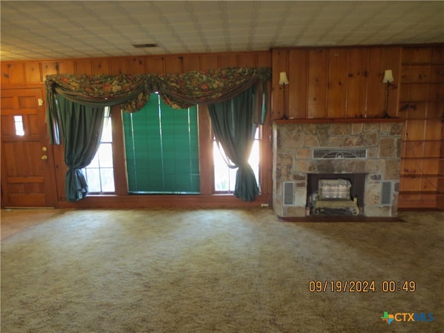 unfurnished living room with carpet flooring, a stone fireplace, and wood walls