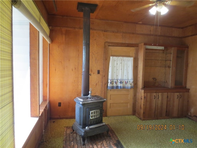 living room featuring carpet, a wood stove, ceiling fan, and wood walls