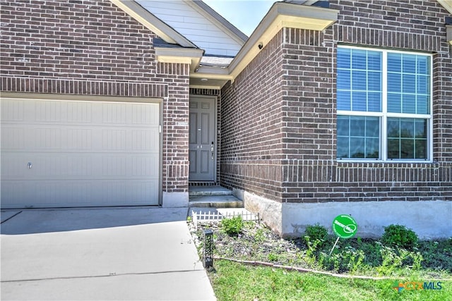 entrance to property with an attached garage, brick siding, and driveway