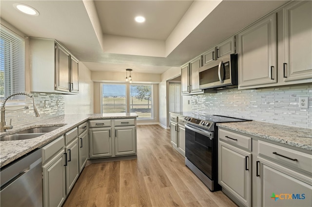 kitchen with gray cabinets, a raised ceiling, sink, light hardwood / wood-style floors, and stainless steel appliances