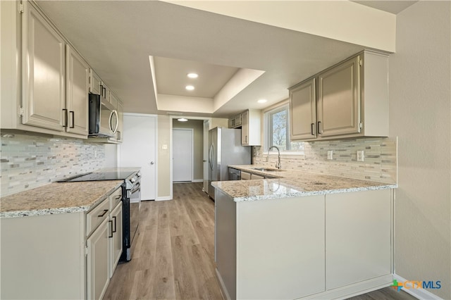 kitchen featuring sink, light hardwood / wood-style flooring, appliances with stainless steel finishes, light stone counters, and kitchen peninsula