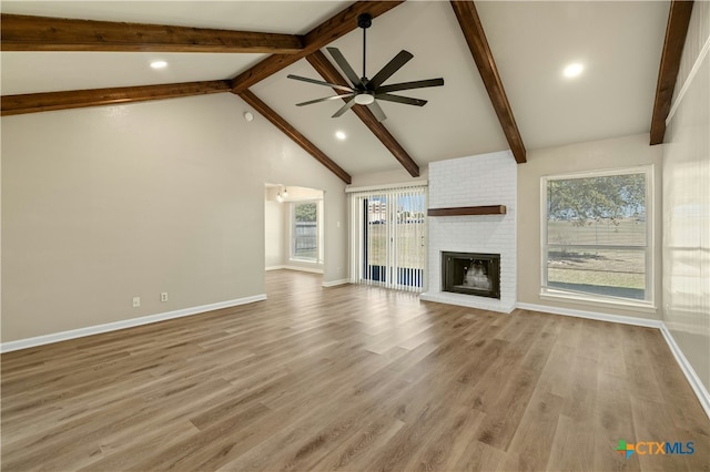 unfurnished living room with high vaulted ceiling, a brick fireplace, beamed ceiling, ceiling fan, and light hardwood / wood-style floors