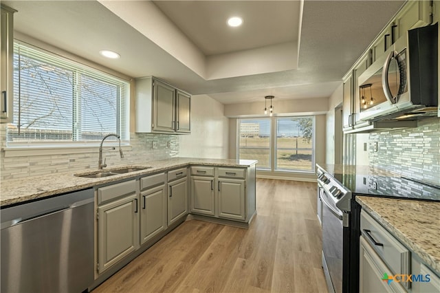 kitchen with sink, light stone counters, a tray ceiling, stainless steel appliances, and light wood-type flooring