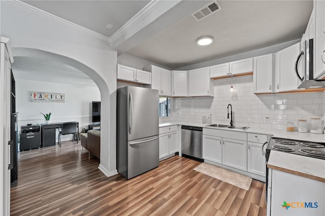 1107 Waco St, Gatesville, TX 76528 - kitchen featuring appliances with stainless steel finishes, a sink, ornamental molding, white cabinets, and arched walkways