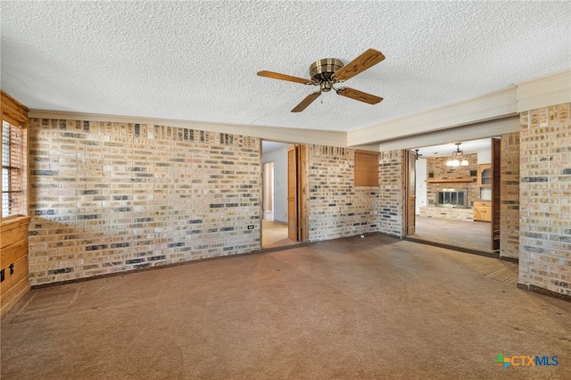 unfurnished living room featuring carpet, a textured ceiling, ceiling fan, and brick wall