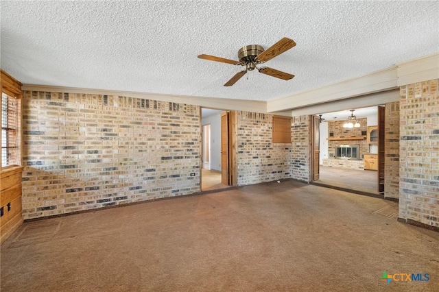 125 Hillview Dr, Luling, TX 78648 - unfurnished living room featuring brick wall, a ceiling fan, a textured ceiling, a fireplace, and carpet flooring