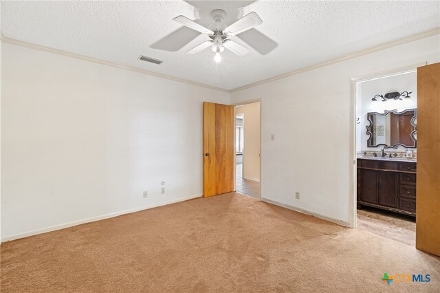 unfurnished bedroom with ornamental molding, ensuite bathroom, ceiling fan, a textured ceiling, and light colored carpet