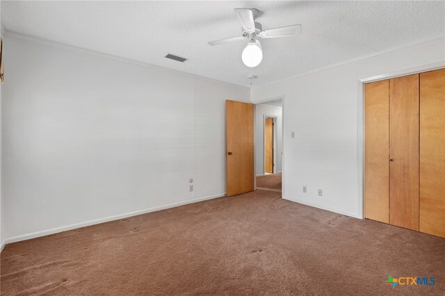 unfurnished bedroom featuring ceiling fan, a textured ceiling, crown molding, a closet, and carpet floors