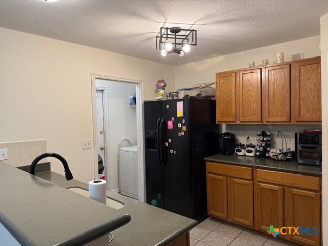 kitchen featuring an inviting chandelier, a textured ceiling, light tile patterned floors, black fridge with ice dispenser, and washer / dryer