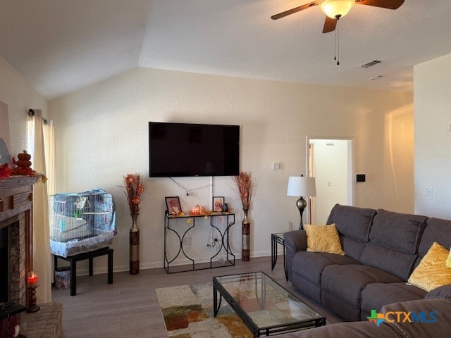 living room with light wood-type flooring, a fireplace, ceiling fan, and vaulted ceiling