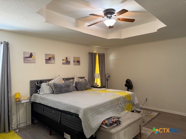 bedroom with hardwood / wood-style flooring, ceiling fan, and a tray ceiling