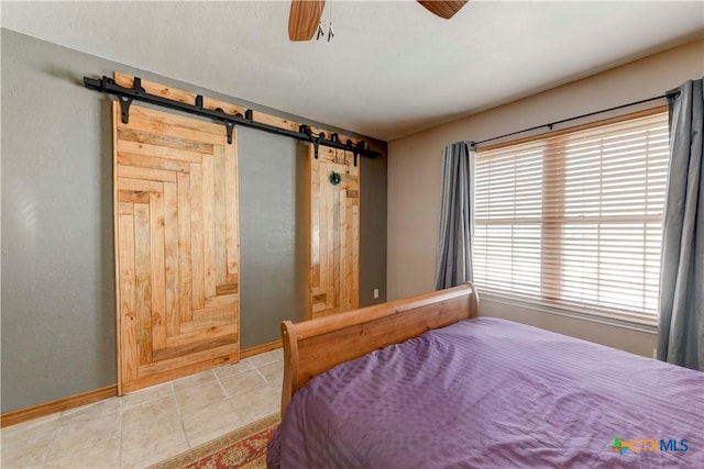 bedroom featuring light tile patterned floors, a barn door, baseboards, and ceiling fan