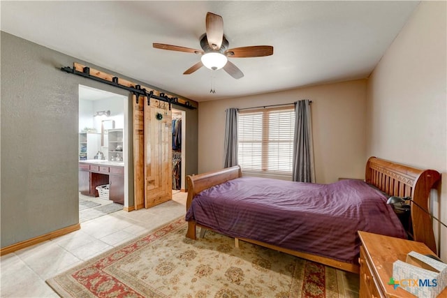 bedroom with a walk in closet, light tile patterned floors, ensuite bathroom, a ceiling fan, and a barn door