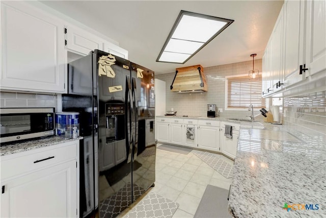 kitchen with light stone counters, a sink, white cabinetry, wall chimney range hood, and stainless steel microwave