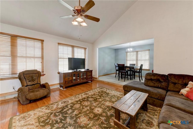 living room featuring baseboards, high vaulted ceiling, wood finished floors, and ceiling fan with notable chandelier