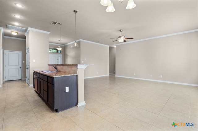 kitchen with light stone counters, ornamental molding, dark brown cabinets, sink, and hanging light fixtures