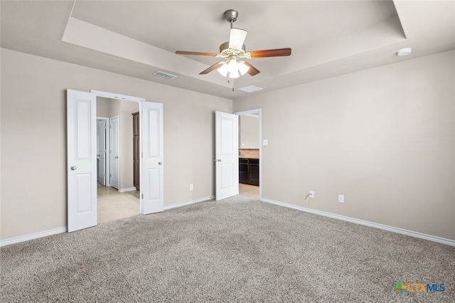 unfurnished bedroom featuring light carpet, ensuite bathroom, a raised ceiling, and ceiling fan