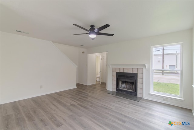 unfurnished living room featuring visible vents, a ceiling fan, wood finished floors, baseboards, and a tile fireplace