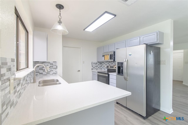 kitchen with backsplash, light wood-type flooring, light countertops, appliances with stainless steel finishes, and a sink