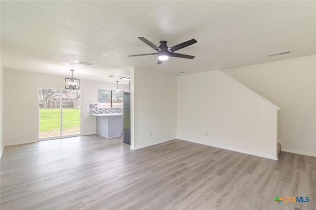 unfurnished living room with visible vents, ceiling fan with notable chandelier, light wood-type flooring, and baseboards