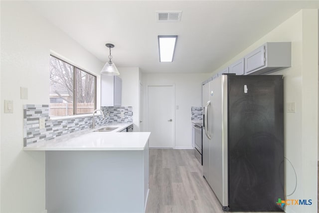 kitchen featuring visible vents, a sink, appliances with stainless steel finishes, a peninsula, and light countertops