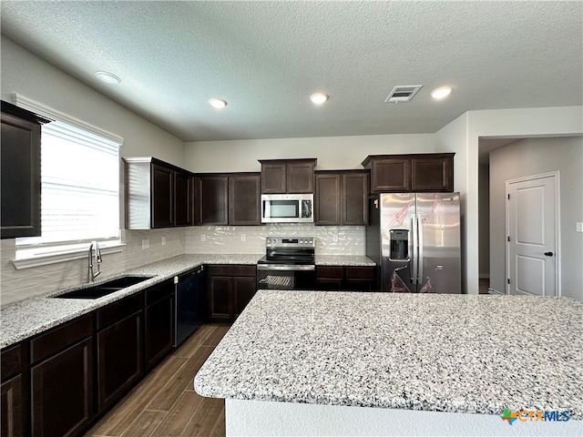 kitchen with dark wood-type flooring, sink, backsplash, light stone countertops, and appliances with stainless steel finishes