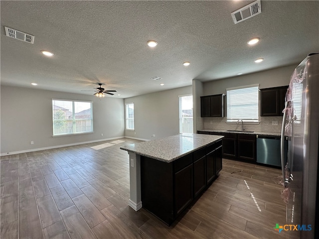 kitchen with stainless steel appliances, a center island, a textured ceiling, dark hardwood / wood-style floors, and ceiling fan