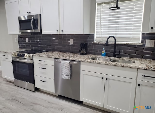 kitchen with stainless steel appliances, sink, light stone counters, white cabinets, and light wood-type flooring