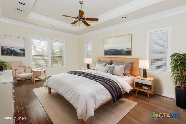 bedroom with a raised ceiling, crown molding, ceiling fan, and dark hardwood / wood-style flooring