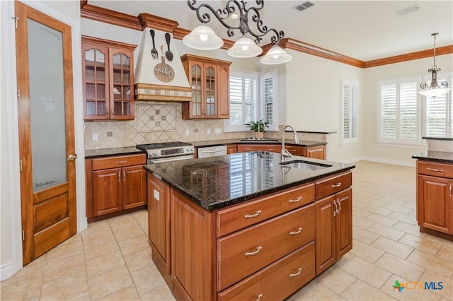 kitchen with sink, appliances with stainless steel finishes, dark stone countertops, ornamental molding, and an island with sink