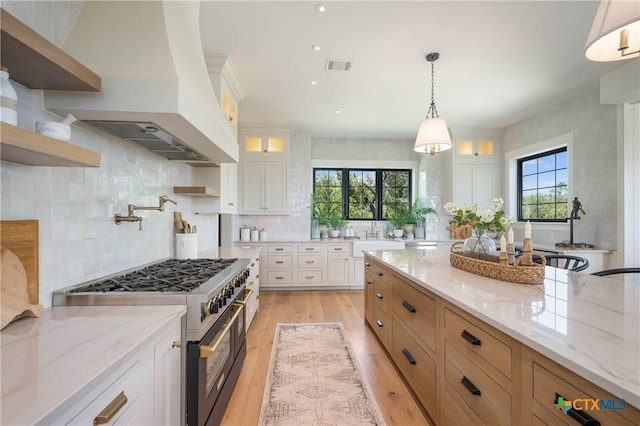 kitchen featuring open shelves, visible vents, premium range hood, light wood-style flooring, and stainless steel range