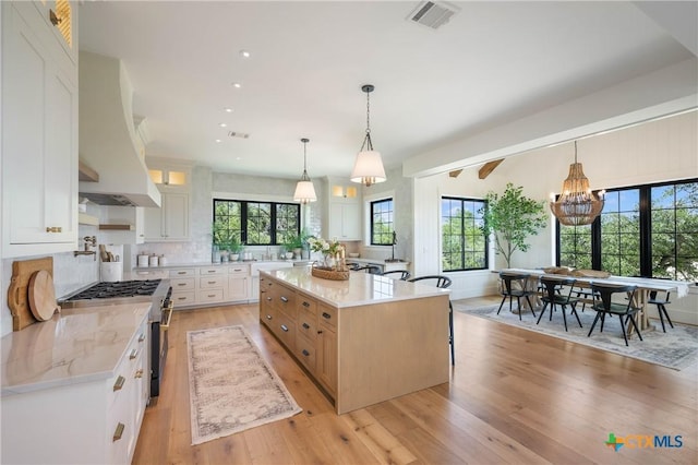 kitchen with white cabinets, high end stainless steel range, visible vents, premium range hood, and glass insert cabinets