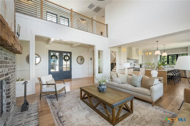 living room with a towering ceiling, visible vents, light wood-type flooring, a decorative wall, and a fireplace
