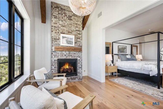 bedroom featuring a chandelier, wood finished floors, multiple windows, and a brick fireplace