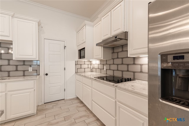 kitchen with black electric cooktop, light stone counters, crown molding, white cabinets, and stainless steel fridge