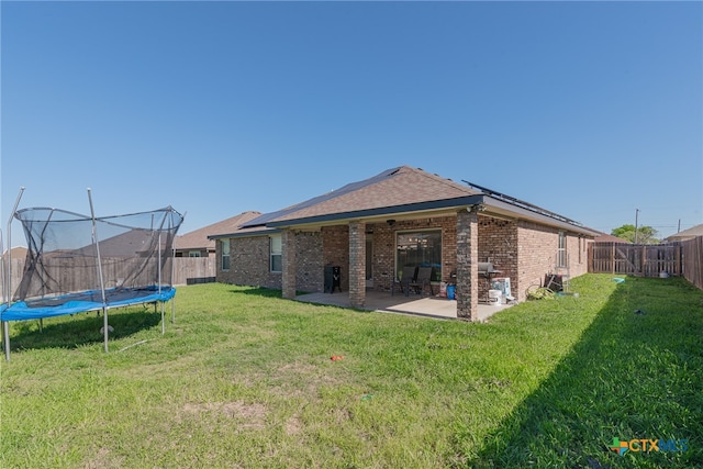 back of house featuring a trampoline, a lawn, and a patio area