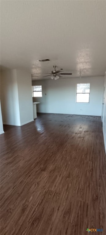 unfurnished living room with a textured ceiling, ceiling fan, and dark wood-type flooring