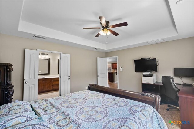 203 Terravista Trl, Victoria, TX 77904 - bedroom featuring a raised ceiling, light colored carpet, ensuite bathroom, a ceiling fan, and an office area