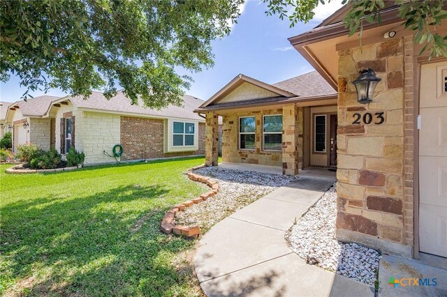 203 Terravista Trl, Victoria, TX 77904 - view of exterior entry with stone siding, a lawn, and roof with shingles