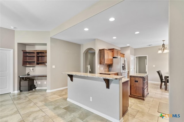 203 Terravista Trl, Victoria, TX 77904 - kitchen with stainless steel fridge with ice dispenser, a kitchen island, light stone counters, brown cabinetry, and a breakfast bar