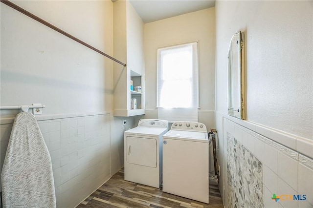 clothes washing area featuring wood finished floors, a wainscoted wall, washing machine and dryer, and tile walls