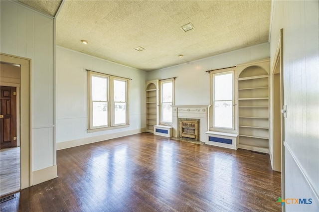 unfurnished living room with a textured ceiling, built in shelves, wood finished floors, and a wealth of natural light