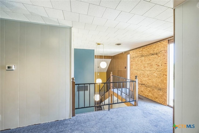hall featuring wooden walls, carpet flooring, and an upstairs landing