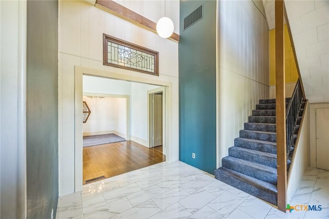 stairway with visible vents, marble finish floor, and a towering ceiling