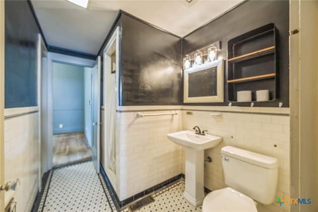 bathroom featuring wainscoting, tile patterned floors, toilet, and tile walls