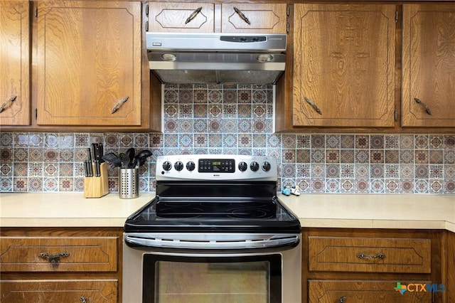 kitchen with brown cabinets, light countertops, electric range, decorative backsplash, and under cabinet range hood