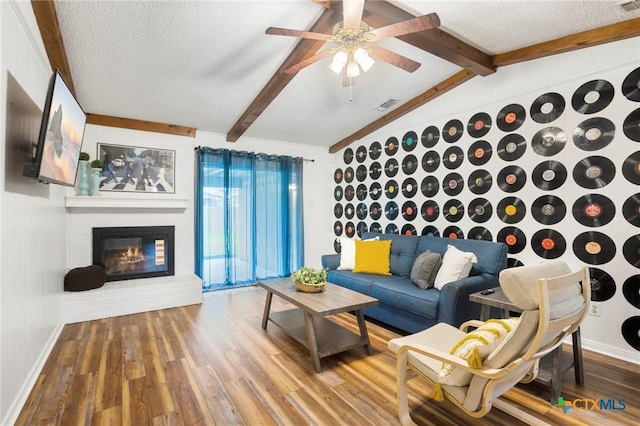 living room featuring lofted ceiling with beams, a brick fireplace, a textured ceiling, and wood finished floors