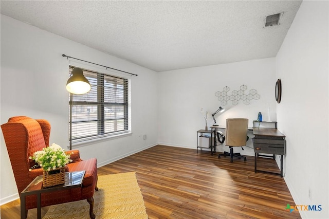 office space featuring baseboards, a textured ceiling, visible vents, and wood finished floors