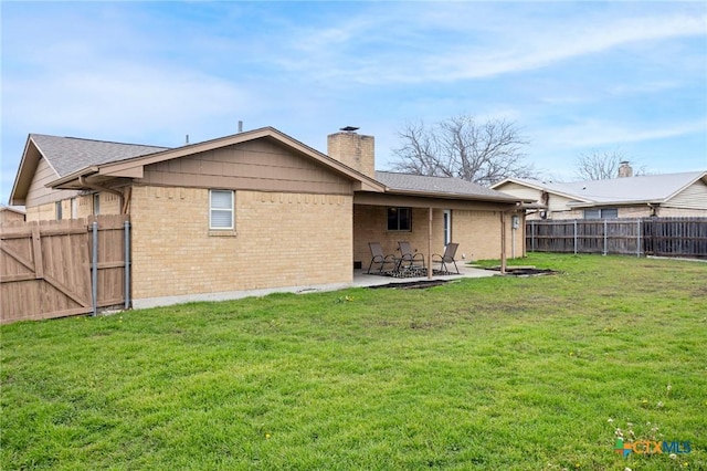 back of house with a yard, a patio, brick siding, and a fenced backyard