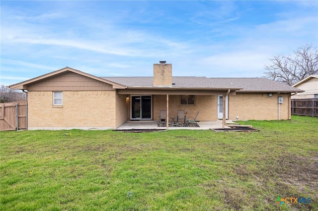 rear view of property featuring a patio, brick siding, fence, a yard, and a chimney